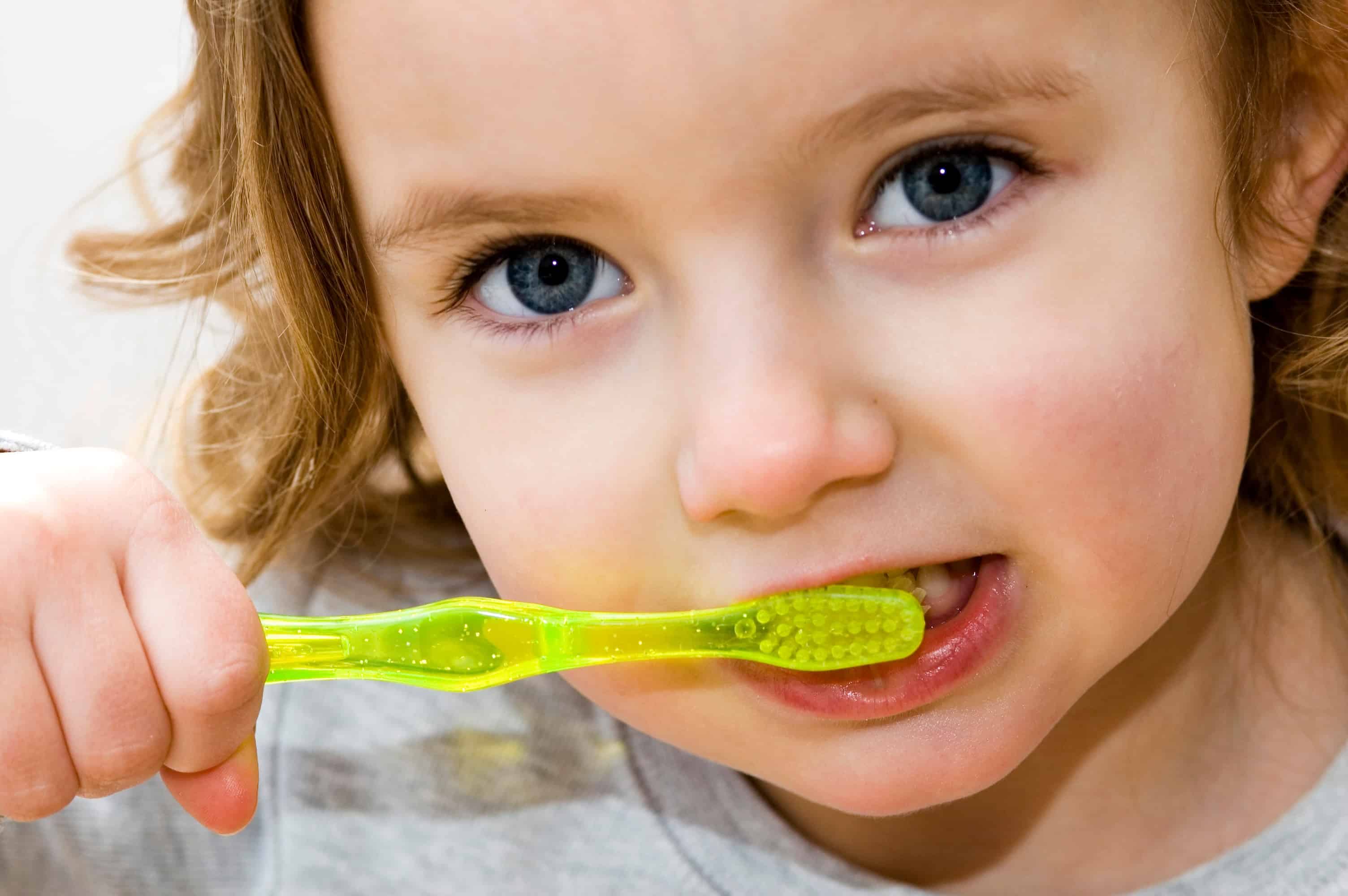 A little girl brushing her teeth against a white background.